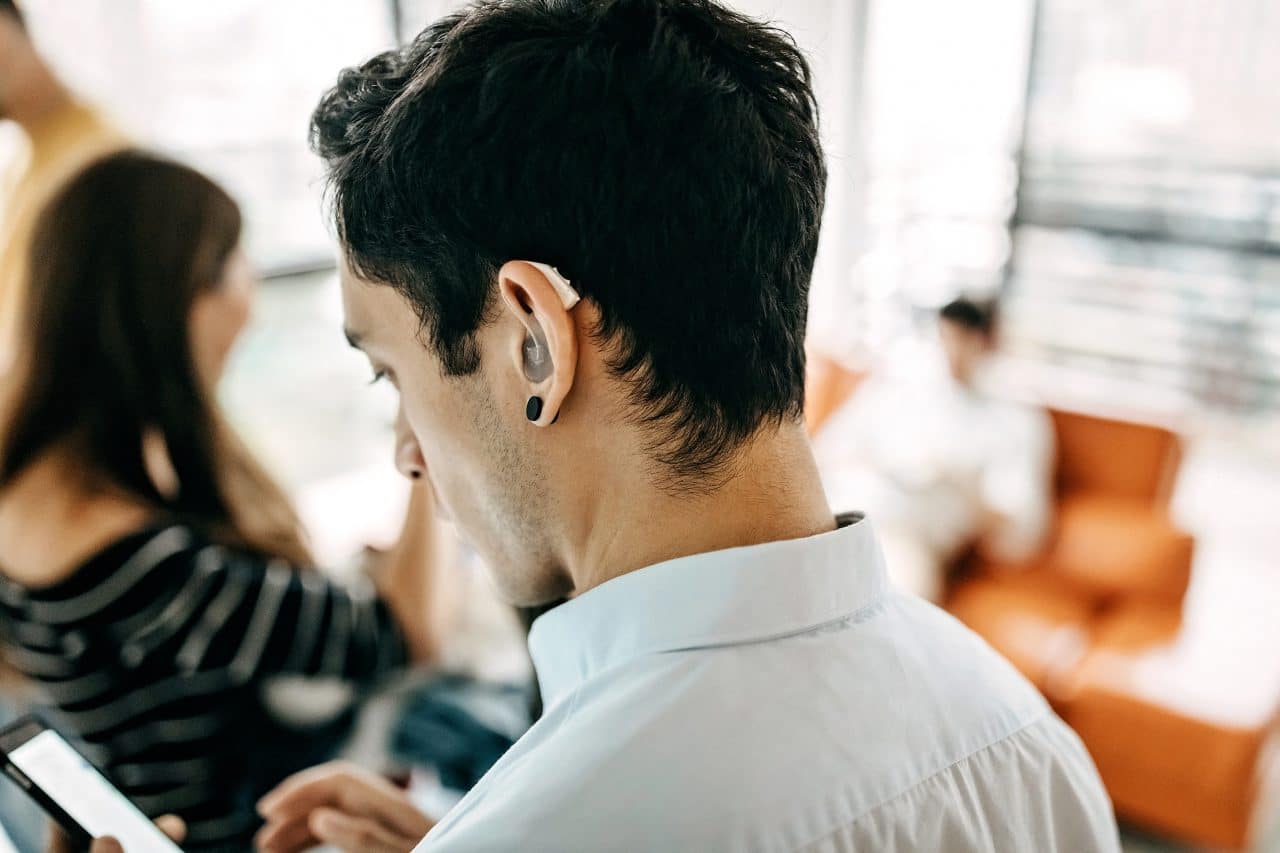 Younger man with a hearing aid uses his smartphone.