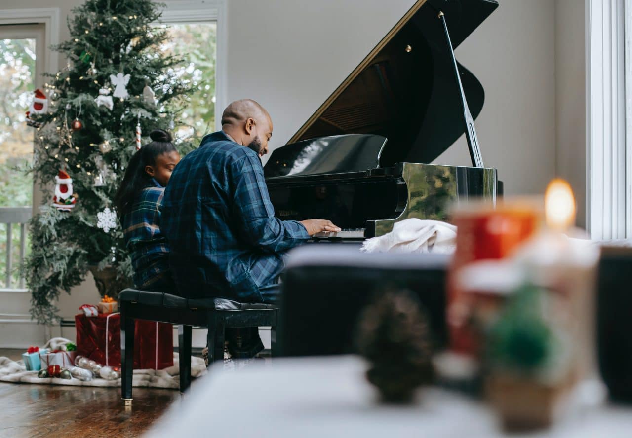 Father and daughter playing piano next to the Christmas tree.