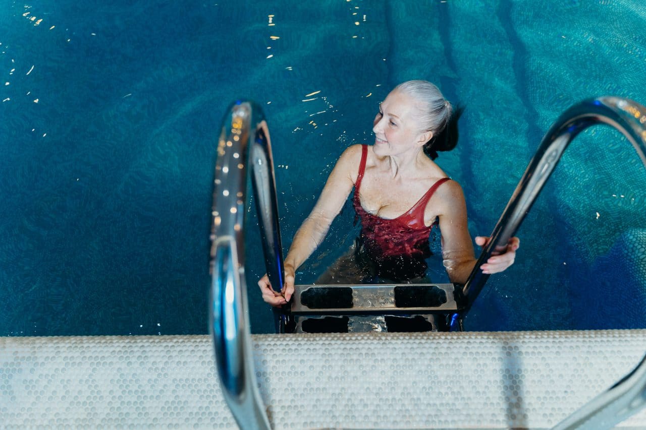 Older woman getting into swimming pool.