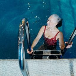 Older woman getting into swimming pool.