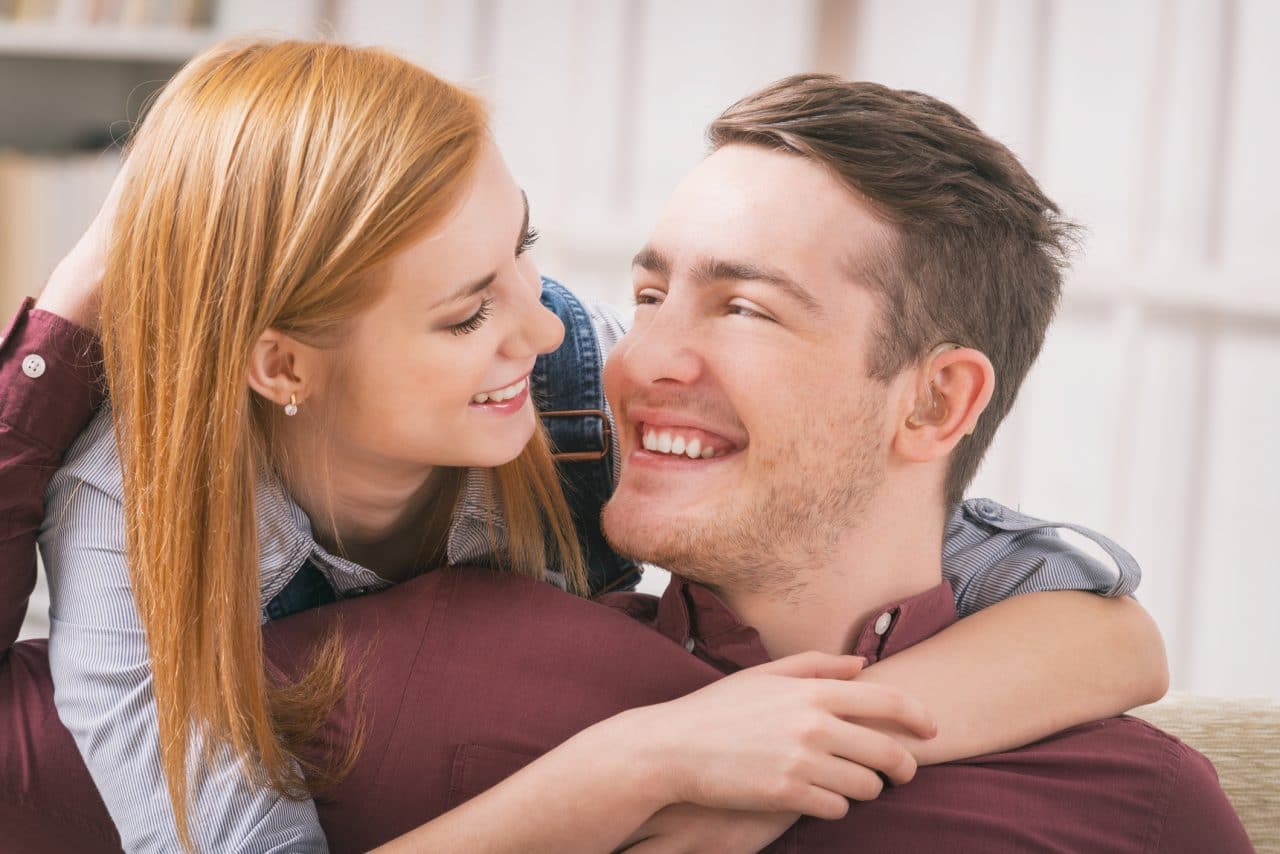 A man wearing hearing aids getting a hug from a woman.