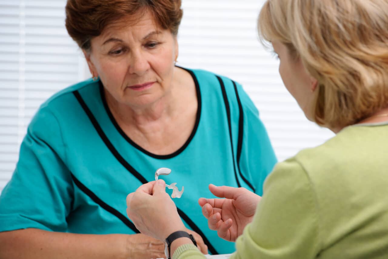 Audiologist showing a senior woman with hearing loss a hearing aid.