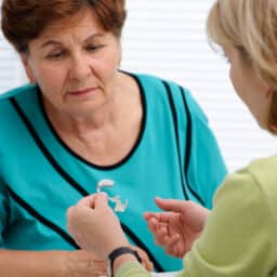 Audiologist showing a senior woman with hearing loss a hearing aid.