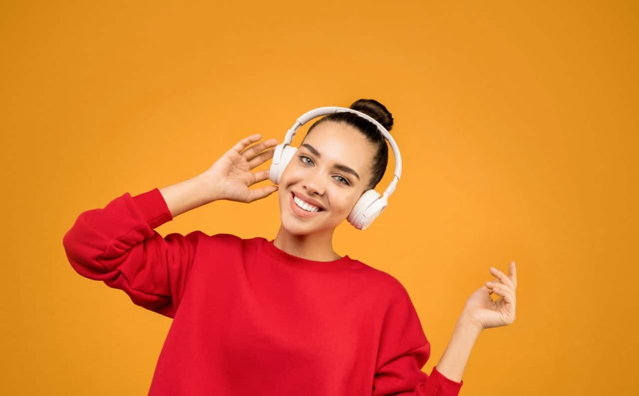 Young woman wearing over-the-ear headphones in front of an orange background/