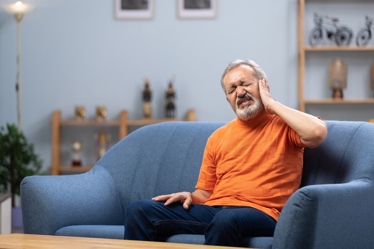 Senior man with ear pain sitting on sofa at home.
