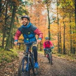 Smiling man biking through the woods with a friend