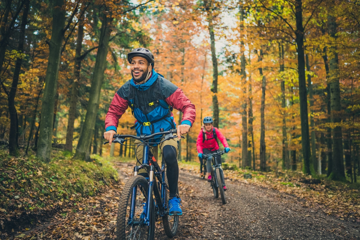 Smiling man biking through the woods with a friend.