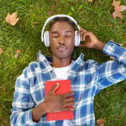 Man enjoys audiobook in headphones holding book outdoor