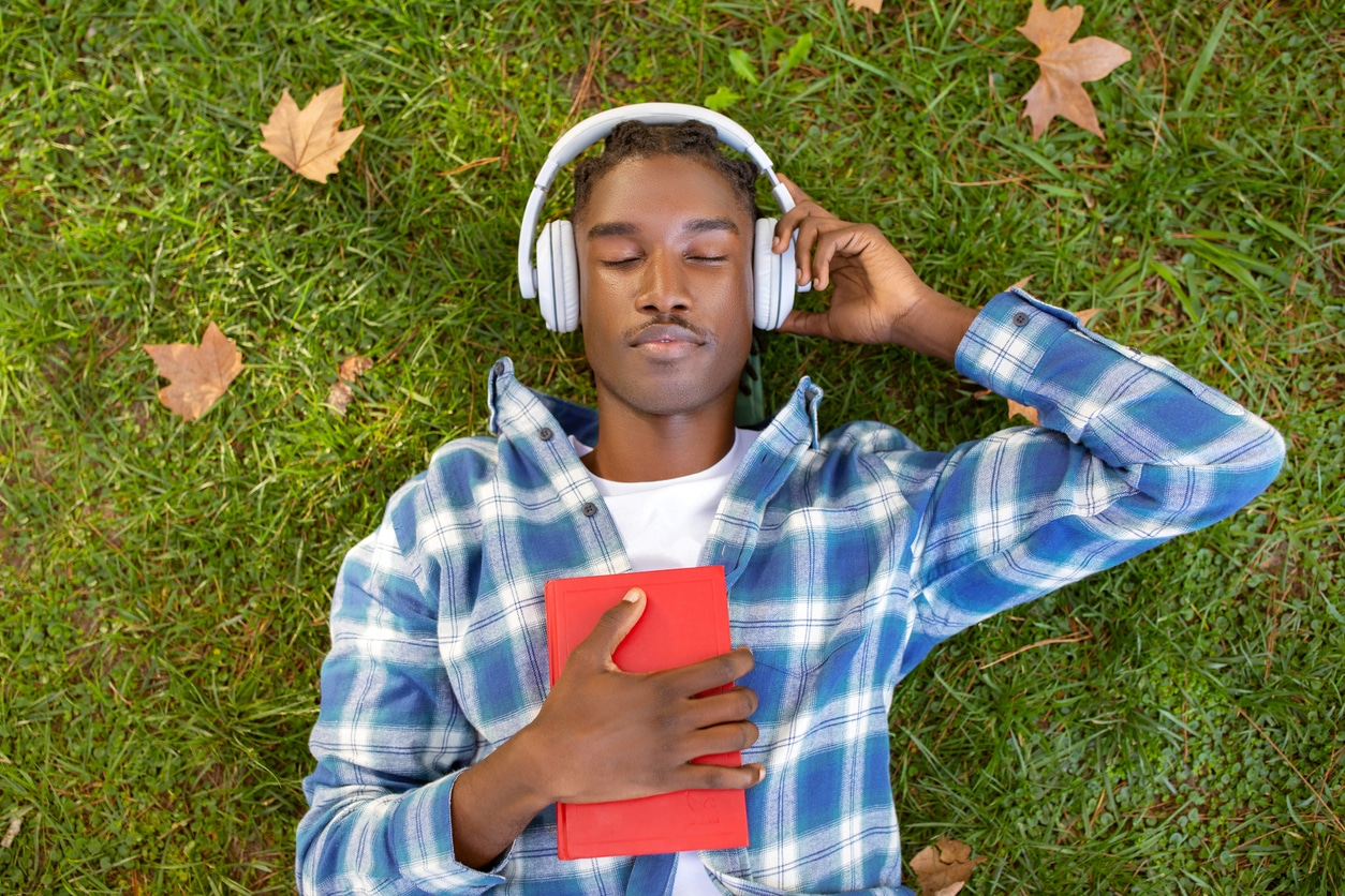 enjoys audiobook in headphones holding book outdoor.